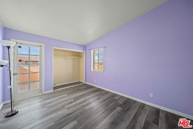 unfurnished bedroom featuring a closet, lofted ceiling, wood-type flooring, and multiple windows