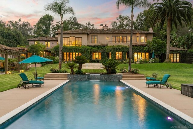 pool at dusk featuring a patio area and a yard