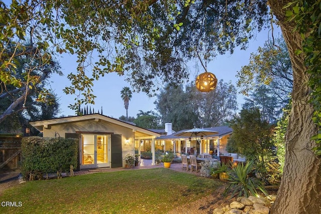 back house at dusk featuring a lawn and a patio