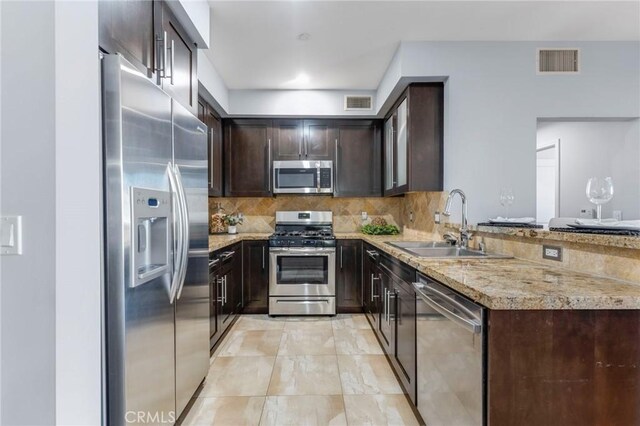 kitchen featuring stainless steel appliances, tasteful backsplash, dark brown cabinets, light stone countertops, and sink