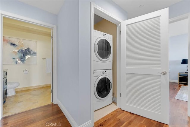 clothes washing area featuring wood-type flooring and stacked washer / dryer