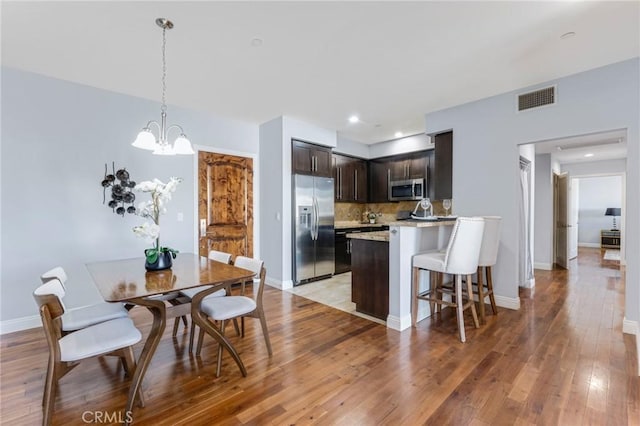 kitchen with dark brown cabinetry, appliances with stainless steel finishes, an inviting chandelier, light hardwood / wood-style floors, and backsplash