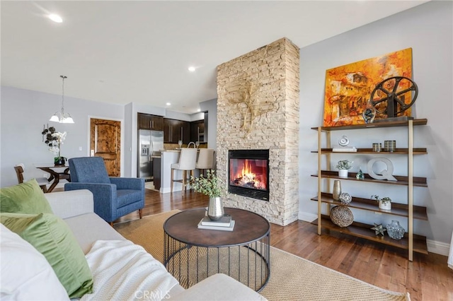 living room featuring dark hardwood / wood-style flooring, a stone fireplace, and a chandelier