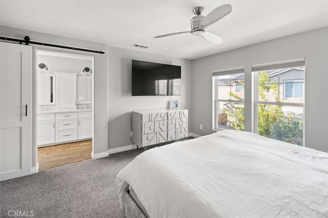 bedroom with ceiling fan, a barn door, carpet flooring, and ensuite bath