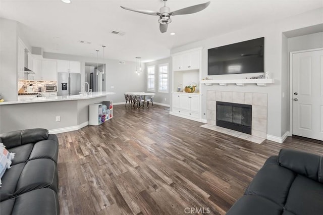 living room featuring dark wood-type flooring, ceiling fan, a tile fireplace, and sink