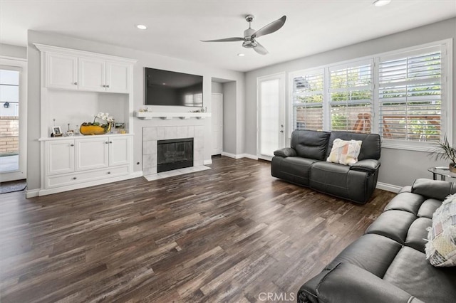 living room with ceiling fan, dark wood-type flooring, and a tiled fireplace