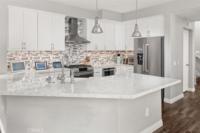 kitchen with pendant lighting, white cabinets, premium appliances, wall chimney exhaust hood, and kitchen peninsula