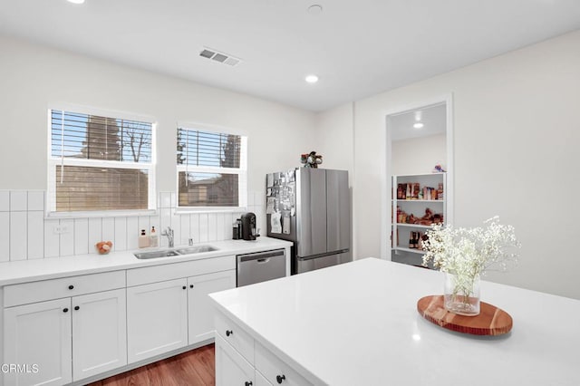 kitchen with light wood-type flooring, appliances with stainless steel finishes, white cabinetry, and sink