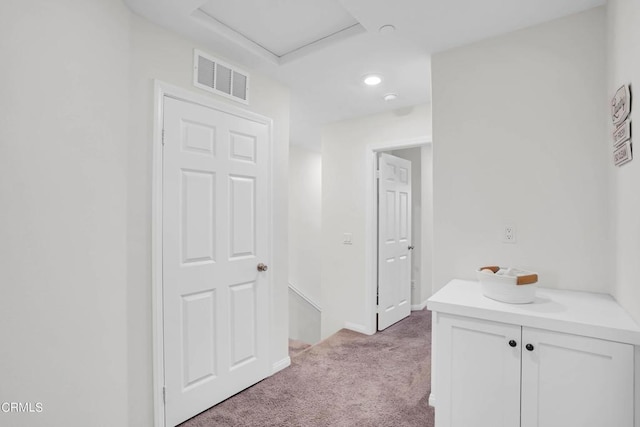 corridor with light colored carpet and a raised ceiling