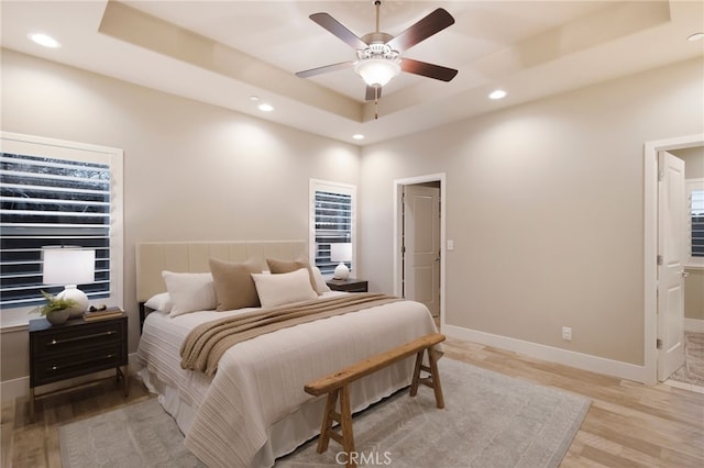 bedroom with ceiling fan, a tray ceiling, and light wood-type flooring