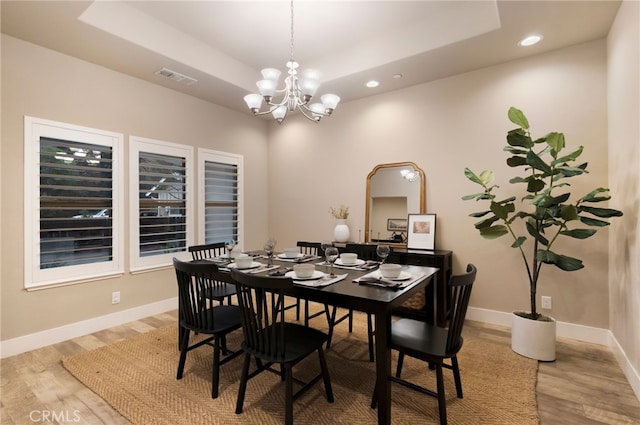 dining room featuring an inviting chandelier, a tray ceiling, and light hardwood / wood-style flooring