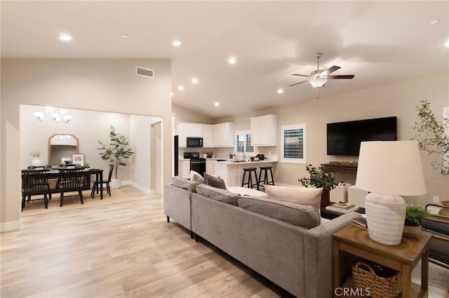 living room featuring light wood-type flooring, vaulted ceiling, and ceiling fan with notable chandelier