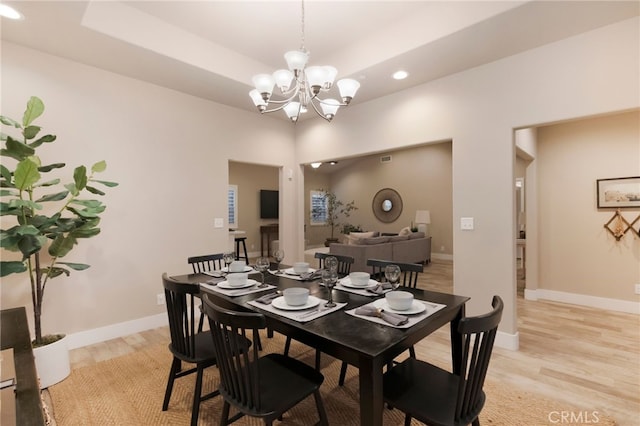 dining area featuring a raised ceiling, light wood-type flooring, and a chandelier