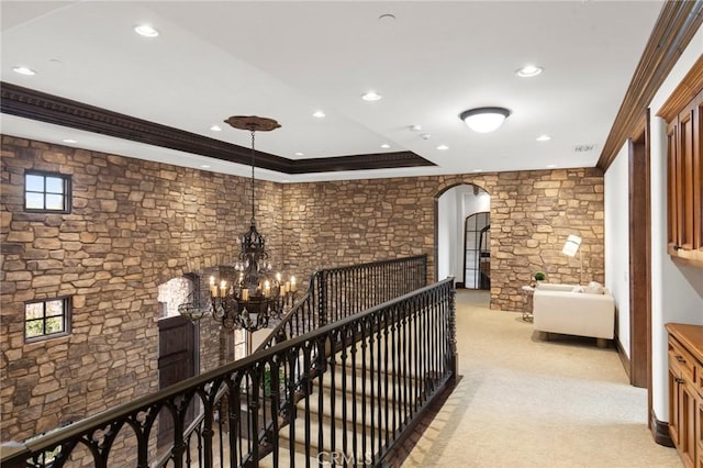 hallway with light carpet, crown molding, a tray ceiling, and a notable chandelier