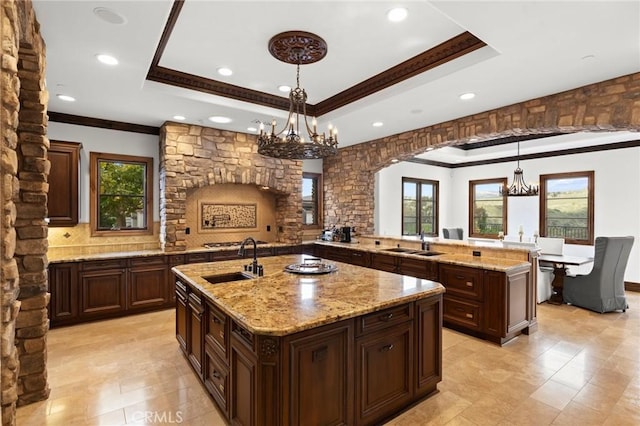 kitchen with decorative light fixtures, sink, a chandelier, and a kitchen island with sink