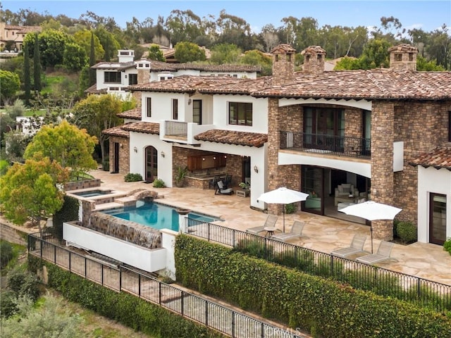 back of house with exterior kitchen, a swimming pool with hot tub, a balcony, and a patio