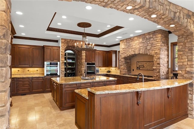 kitchen featuring a large island, stainless steel double oven, hanging light fixtures, light stone countertops, and crown molding