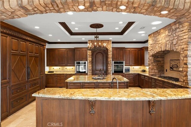 kitchen with light stone countertops, pendant lighting, tasteful backsplash, a raised ceiling, and ornamental molding