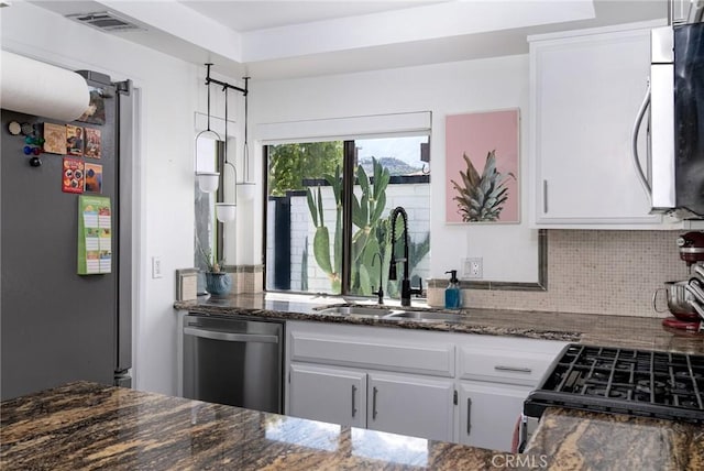 kitchen with appliances with stainless steel finishes, tasteful backsplash, sink, dark stone countertops, and white cabinets