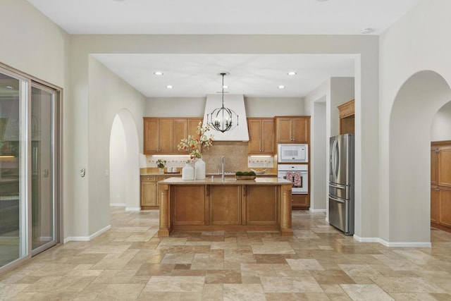 kitchen featuring white appliances, an island with sink, decorative backsplash, hanging light fixtures, and a chandelier