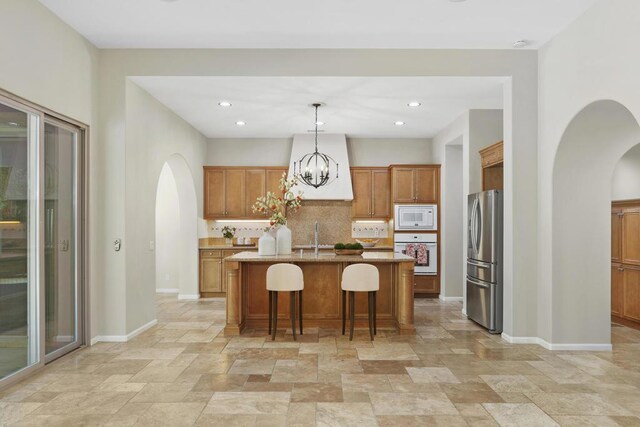 kitchen featuring white appliances, an inviting chandelier, an island with sink, a kitchen breakfast bar, and hanging light fixtures