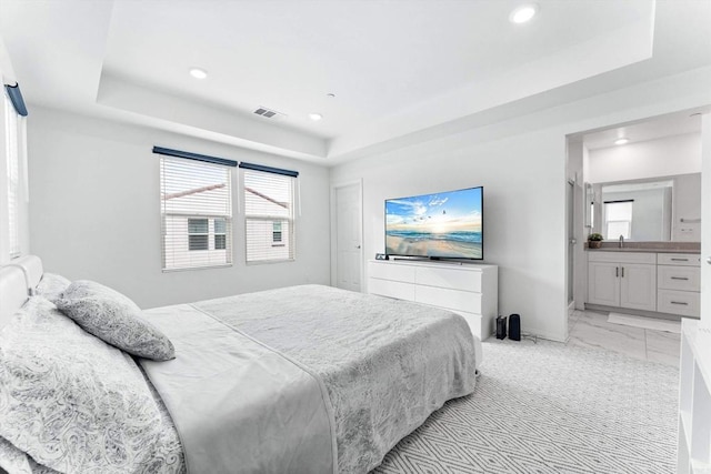 bedroom featuring connected bathroom, a tray ceiling, and sink