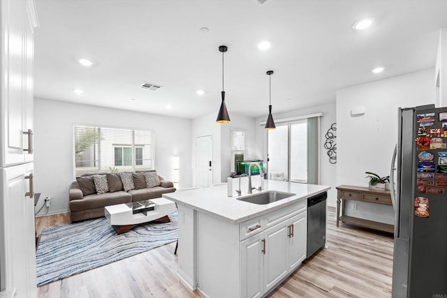 kitchen with an island with sink, appliances with stainless steel finishes, pendant lighting, white cabinets, and sink