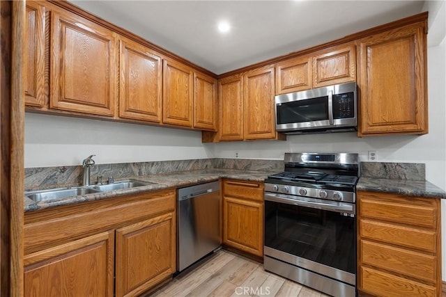 kitchen featuring stainless steel appliances, light hardwood / wood-style flooring, dark stone counters, and sink