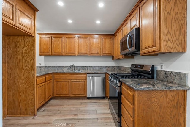 kitchen with stainless steel appliances, light hardwood / wood-style flooring, dark stone counters, and sink