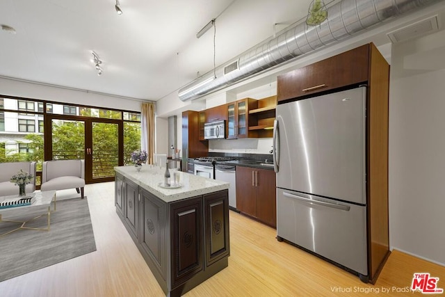 kitchen with appliances with stainless steel finishes, light wood-type flooring, dark brown cabinets, french doors, and a kitchen island