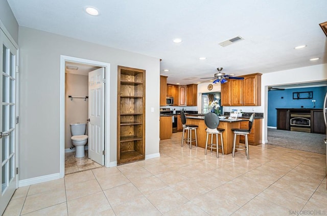 kitchen with ceiling fan, a kitchen island, a kitchen bar, stainless steel appliances, and built in shelves