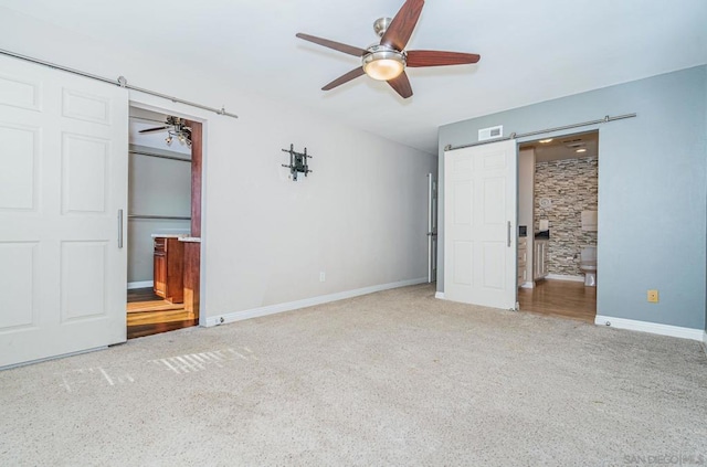 unfurnished bedroom featuring ceiling fan, a barn door, carpet floors, and ensuite bath