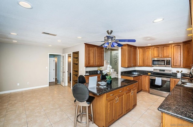 kitchen featuring sink, appliances with stainless steel finishes, light tile patterned flooring, and dark stone countertops