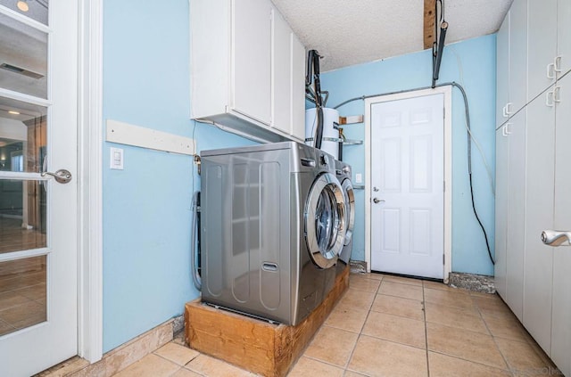 laundry area with a textured ceiling, cabinets, washer and dryer, and light tile patterned floors