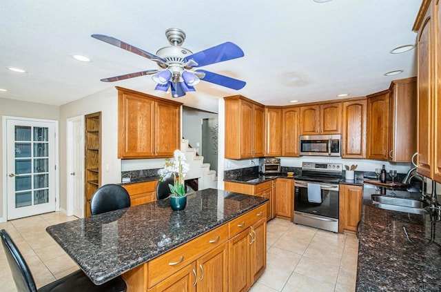 kitchen featuring ceiling fan, dark stone countertops, sink, stainless steel appliances, and light tile patterned floors