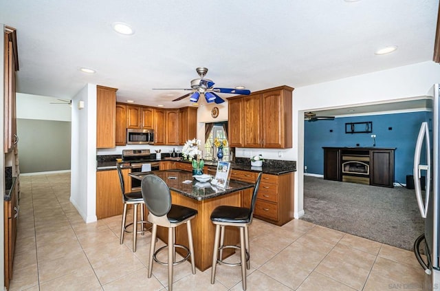 kitchen featuring light carpet, a breakfast bar area, stainless steel appliances, dark stone counters, and a center island