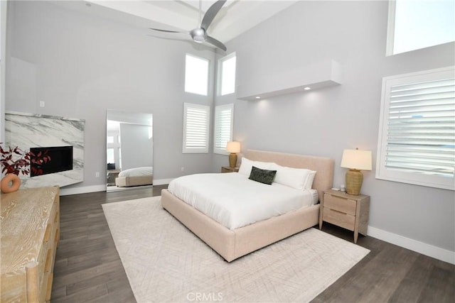 bedroom featuring ceiling fan, dark hardwood / wood-style flooring, a fireplace, and a high ceiling