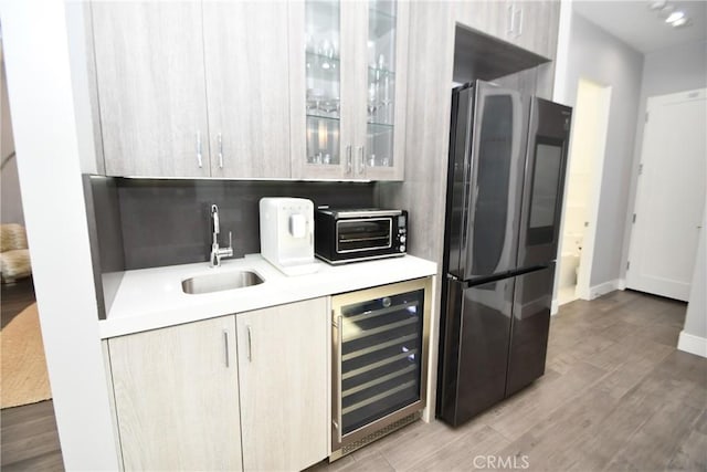 kitchen featuring hardwood / wood-style floors, black fridge, sink, light brown cabinets, and beverage cooler