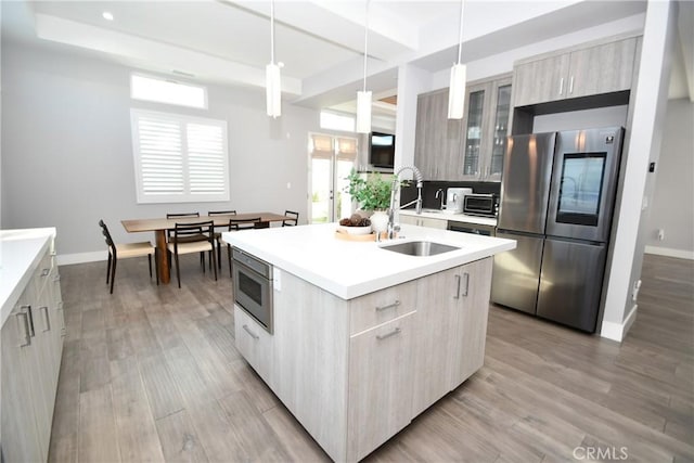 kitchen featuring decorative light fixtures, sink, stainless steel refrigerator, a kitchen island with sink, and light brown cabinetry