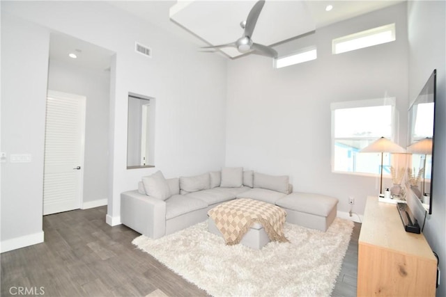 living room with ceiling fan, dark hardwood / wood-style flooring, a healthy amount of sunlight, and a towering ceiling