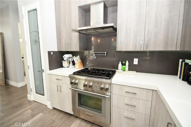 kitchen featuring wall chimney exhaust hood, light brown cabinets, decorative backsplash, high end stove, and light wood-type flooring