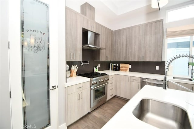 kitchen with high end stainless steel range oven, tasteful backsplash, light brown cabinetry, wall chimney range hood, and light hardwood / wood-style flooring