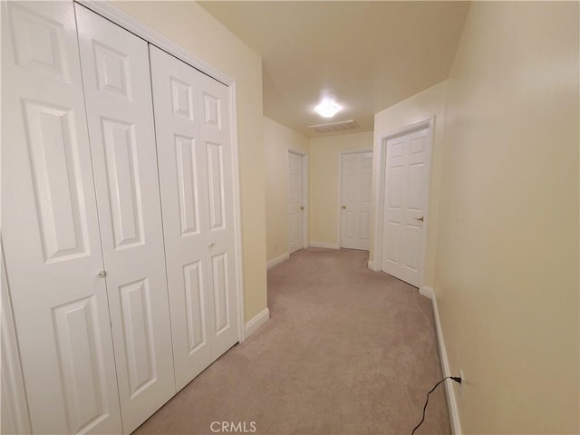 corridor with light colored carpet, visible vents, and baseboards