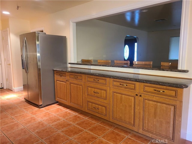 kitchen featuring light tile patterned floors, arched walkways, visible vents, stainless steel fridge with ice dispenser, and brown cabinetry