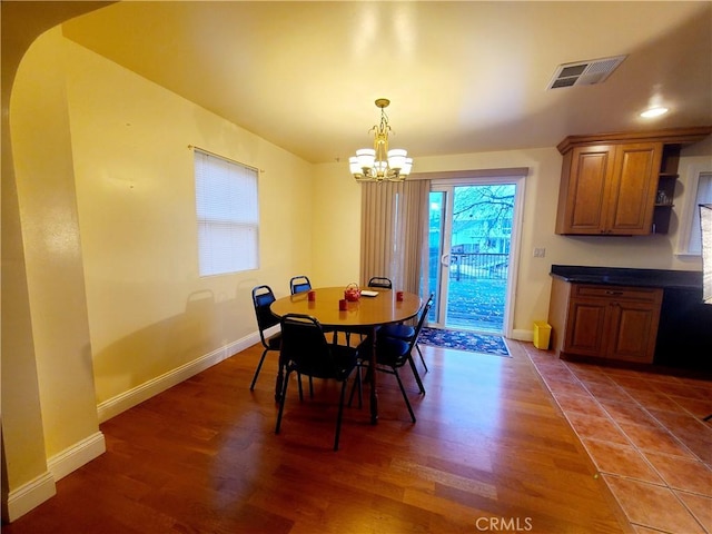 dining space featuring baseboards, wood finished floors, visible vents, and an inviting chandelier