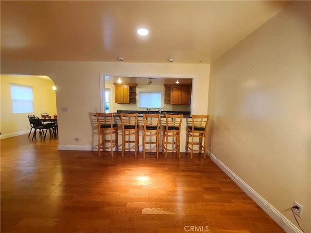 kitchen with light wood-style floors, arched walkways, a breakfast bar, and baseboards