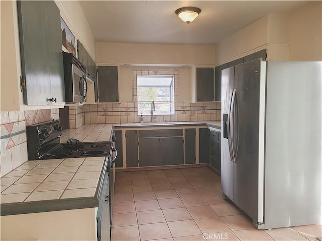 kitchen with stainless steel appliances, tile countertops, sink, light tile patterned flooring, and tasteful backsplash