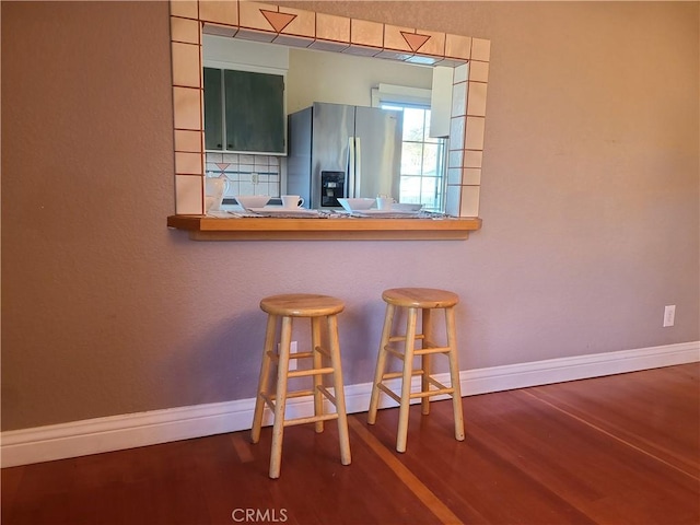 kitchen featuring decorative backsplash, a kitchen bar, hardwood / wood-style floors, and stainless steel fridge with ice dispenser