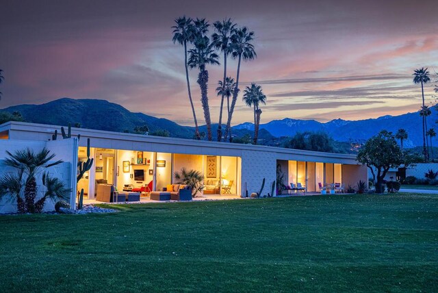 back house at dusk with an outdoor living space, a mountain view, and a lawn