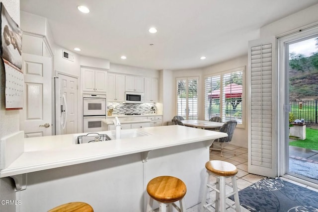 kitchen with sink, white appliances, a breakfast bar, white cabinets, and kitchen peninsula